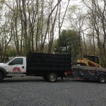 A truck with a trailer loading a cat machine with trees in the background