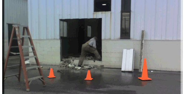 A man is working on a building with orange cones.