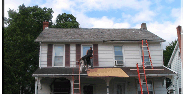 A man on a ladder on the roof of a house.